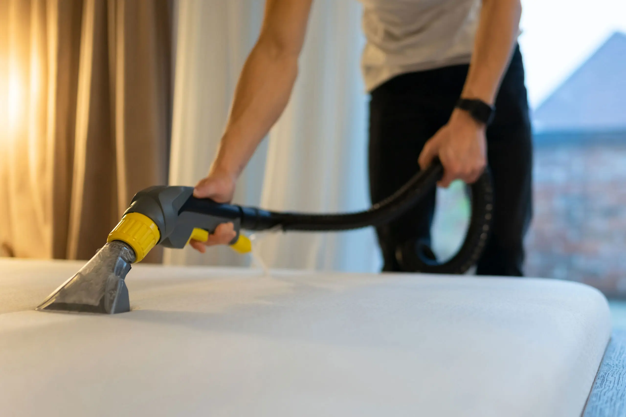 Person cleaning a mattress with a professional vacuum tool to remove bed bugs and allergens.